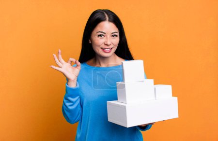 Téléchargez les photos : Hispanic pretty woman feeling happy, showing approval with okay gesture. with white boxes packagings - en image libre de droit