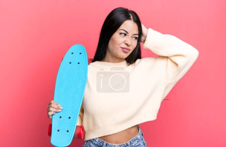 Photo for Hispanic pretty woman feeling puzzled and confused, scratching head. skate boarding concept - Royalty Free Image