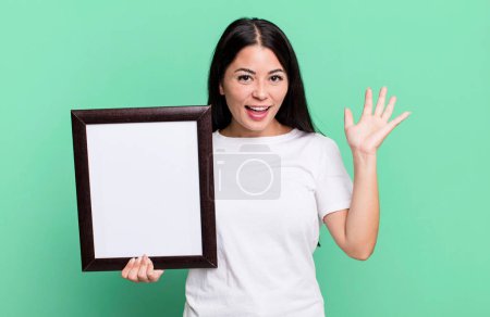 Photo for Hispanic pretty woman feeling happy, surprised realizing a solution or idea with an empty blank frame - Royalty Free Image
