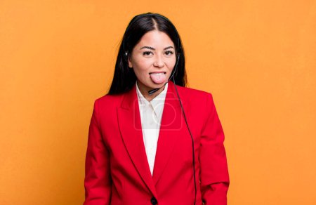 Foto de Hispanic pretty woman with cheerful and rebellious attitude, joking and sticking tongue out. telemarketing concept - Imagen libre de derechos