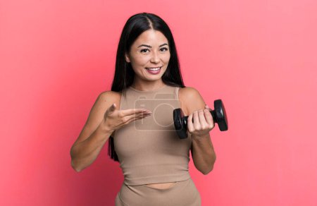 Téléchargez les photos : Hispanique jolie femme souriant joyeusement, se sentant heureux et montrant un concept. concept de fitness et haltère - en image libre de droit