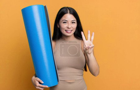 Foto de Mujer bonita hispana sonriendo y luciendo amigable, mostrando el concepto número tres de yoga - Imagen libre de derechos