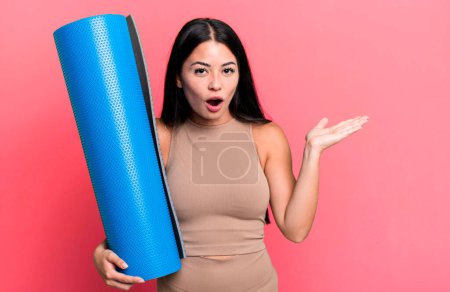 Foto de Hispanic pretty woman looking surprised and shocked, with jaw dropped holding an object yoga concept - Imagen libre de derechos