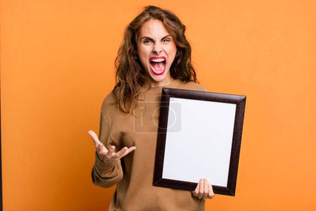 Photo for Hispanic pretty woman looking angry, annoyed and frustrated with an empty blank frame - Royalty Free Image