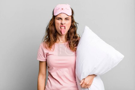 Foto de Hispanic pretty woman feeling disgusted and irritated and tongue out wearing pajamas and a pillow - Imagen libre de derechos