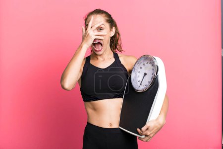 Téléchargez les photos : Hispanic pretty woman looking shocked, scared or terrified, covering face with hand. fitness, diet and weight scale concept - en image libre de droit
