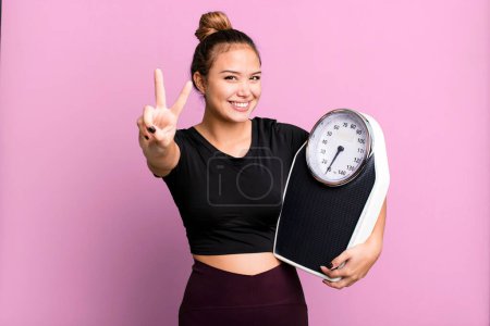Photo for Hispanic pretty woman smiling and looking happy, gesturing victory or peace. fitness and diet concept - Royalty Free Image