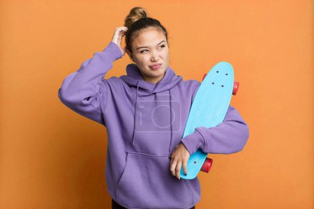 Photo for Hispanic pretty woman feeling puzzled and confused, scratching head. skate boarding concept - Royalty Free Image