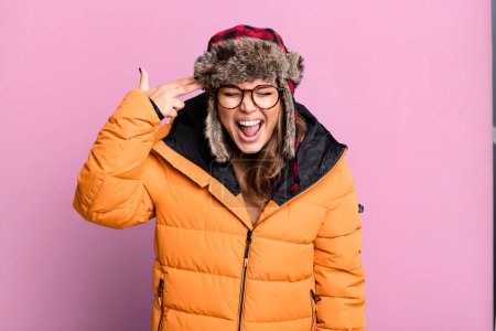 Photo for Hispanic pretty woman looking unhappy and stressed, suicide gesture making gun sign wearing anorak. cold and winter concept - Royalty Free Image