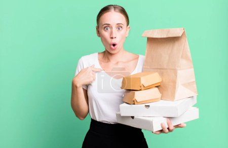 Photo for Caucasian pretty woman looking shocked and surprised with mouth wide open, pointing to self. with fast food packages. delivery concept - Royalty Free Image