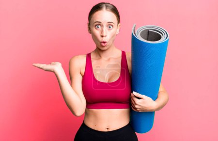 Foto de Caucasian pretty woman looking surprised and shocked, with jaw dropped holding an object. fitness and yoga concept - Imagen libre de derechos