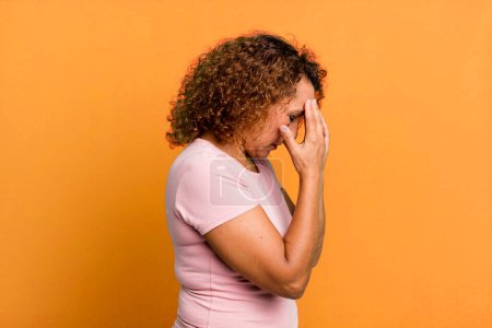 Foto de Mujer hispana de mediana edad cubriendo los ojos con las manos con una mirada triste y frustrada de desesperación, llanto, vista lateral - Imagen libre de derechos
