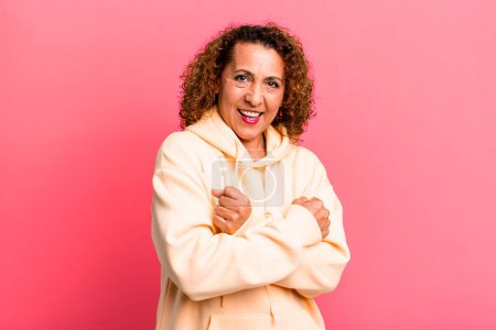 Téléchargez les photos : Femme hispanique d'âge moyen souriant joyeusement et célébrant, avec les poings serrés et les bras croisés, se sentant heureux et positif - en image libre de droit
