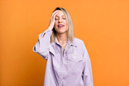 Photo for Blonde adult woman laughing and slapping forehead like saying doh! I forgot or that was a stupid mistake - Royalty Free Image