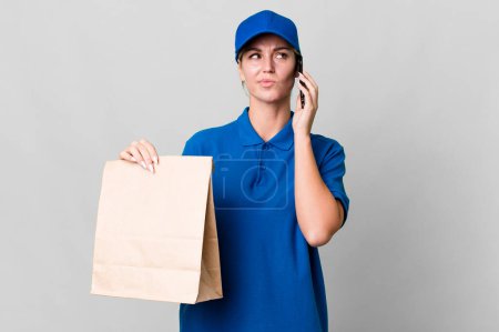 Foto de Pretty caucasian  delivery woman with a paper bag and a phone - Imagen libre de derechos
