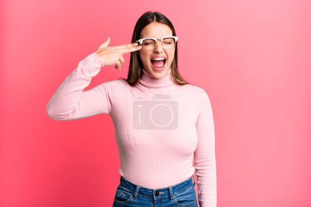 Foto de Pretty young adult woman looking unhappy and stressed, suicide gesture making gun sign with hand, pointing to head - Imagen libre de derechos