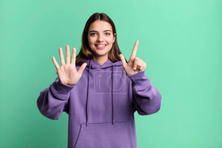 Téléchargez les photos : Pretty young adult woman smiling and looking friendly, showing number seven or seventh with hand forward, counting down - en image libre de droit