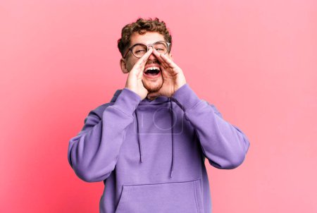 Photo for Young adult caucasian man feeling happy, excited and positive, giving a big shout out with hands next to mouth, calling out - Royalty Free Image