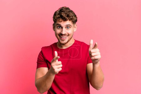 Photo for Young adult caucasian man smiling with a positive, successful, happy attitude pointing to the camera, making gun sign with hands - Royalty Free Image