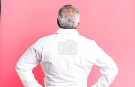 Foto de Hombre mayor de mediana edad sintiéndose confundido o lleno de dudas y preguntas, preguntándose, con las manos en las caderas, vista trasera - Imagen libre de derechos