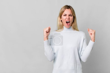 Foto de Caucasian blonde woman shouting aggressively with an angry expression. copy space concept - Imagen libre de derechos