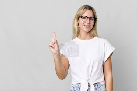 Photo for Caucasian blonde woman smiling and looking friendly, showing number one. copy space concept - Royalty Free Image