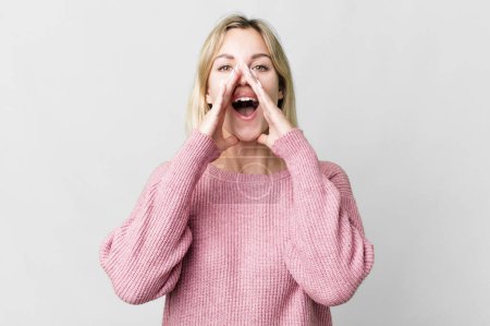 Photo for Caucasian blonde woman feeling happy,giving a big shout out with hands next to mouth - Royalty Free Image