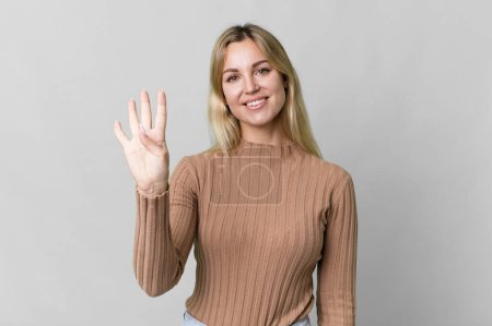 Foto de Caucasian blonde woman smiling and looking friendly, showing number four - Imagen libre de derechos
