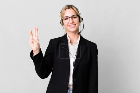 Foto de Caucasian blonde woman smiling and looking friendly, showing number three. telemarketing cocnept - Imagen libre de derechos