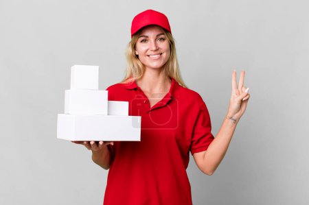 Téléchargez les photos : Caucasian blonde woman smiling and looking friendly, showing number two. delivery boxes - en image libre de droit