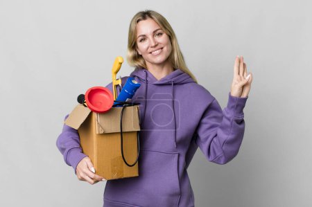 Foto de Caucasian blonde woman smiling and looking friendly, showing number four. housekeeper concept - Imagen libre de derechos