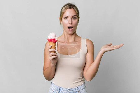 Foto de Caucasian blonde woman looking surprised and shocked, with jaw dropped holding an object. ice cream concept - Imagen libre de derechos