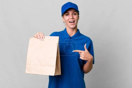 Téléchargez les photos : Caucasian blonde woman looking excited and surprised pointing to the side. paper bag delivery concept - en image libre de droit