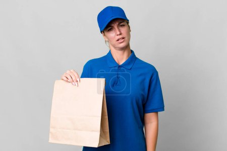 Foto de Caucasian blonde woman feeling puzzled and confused. paper bag delivery concept - Imagen libre de derechos