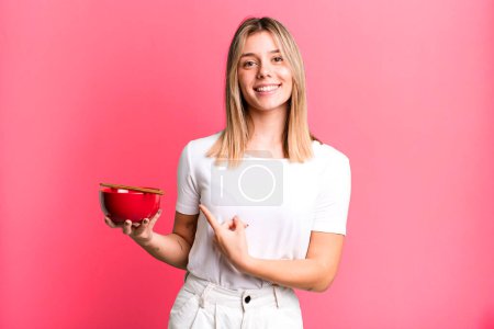 Photo for Young pretty woman smiling cheerfully, feeling happy and pointing to the side. japanese ramen noodles concept - Royalty Free Image