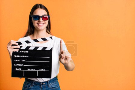Photo for Young pretty woman smiling proudly and confidently making number one. cinema film or movie concept - Royalty Free Image