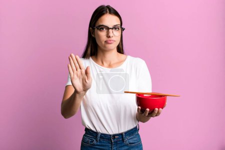 Photo for Young pretty woman looking serious showing open palm making stop gesture. japanese ramen noodles concept - Royalty Free Image