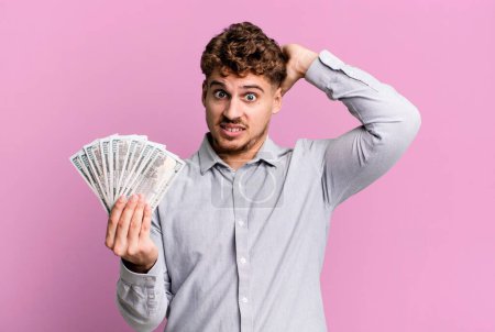 Foto de Young adult caucasian man feeling stressed, anxious or scared, with hands on head. dollar bank notes concept - Imagen libre de derechos
