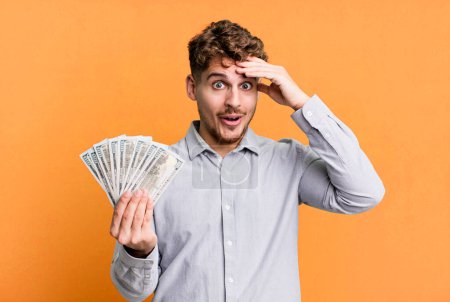 Foto de Young adult caucasian man looking happy, astonished and surprised. dollar bank notes concept - Imagen libre de derechos