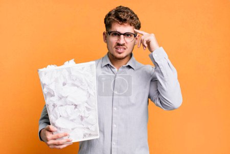 Photo for Young adult caucasian man feeling confused and puzzled, showing you are insane with a paper balls trash concept - Royalty Free Image