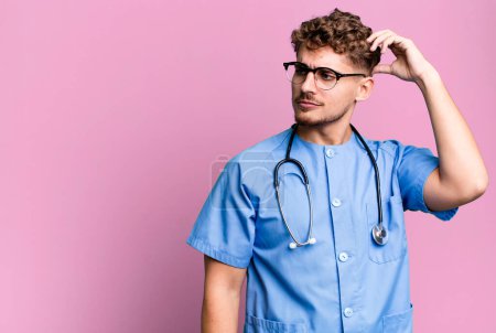 Téléchargez les photos : Young adult caucasian man smiling happily and daydreaming or doubting. nurse concept - en image libre de droit