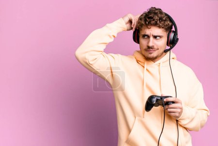 Foto de Young adult caucasian man smiling happily and daydreaming or doubting with headset and a controller. gamer concept - Imagen libre de derechos