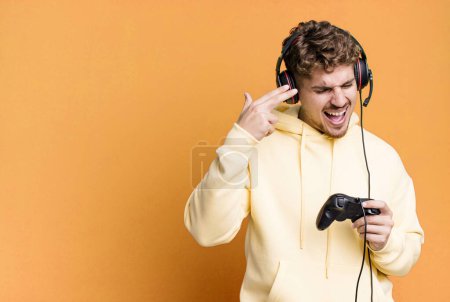 Photo for Young adult caucasian man looking unhappy and stressed, suicide gesture making gun sign with headset and a controller. gamer concept - Royalty Free Image