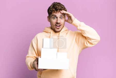 Photo for Young adult caucasian man looking happy, astonished and surprised. blank different packages concept - Royalty Free Image