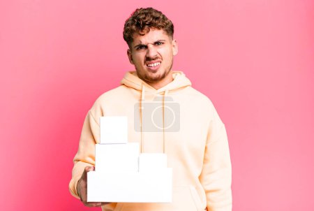 young adult caucasian man feeling puzzled and confused. blank different packages concept