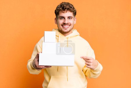 Photo for Young adult caucasian man smiling cheerfully, feeling happy and pointing to the side. blank different packages concept - Royalty Free Image