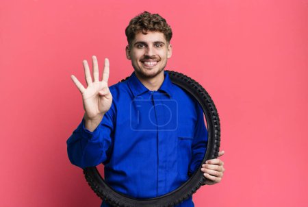 Photo for Young adult caucasian man smiling and looking friendly, showing number four. bike repairman or mechanic concept - Royalty Free Image