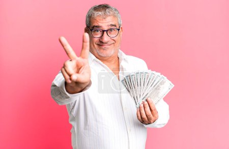 Photo for Middle age senior man smiling and looking happy, gesturing victory or peace. dollar banknotes concept - Royalty Free Image