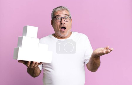 Téléchargez les photos : Homme âgé d'âge moyen regardant surpris et choqué, avec la mâchoire tombée tenant un objet. différents paquets boîtes vides - en image libre de droit
