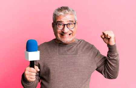 Foto de Hombre mayor de mediana edad gritando agresivamente con una expresión de enojo. periodista o presentador de televisión con un micro - Imagen libre de derechos